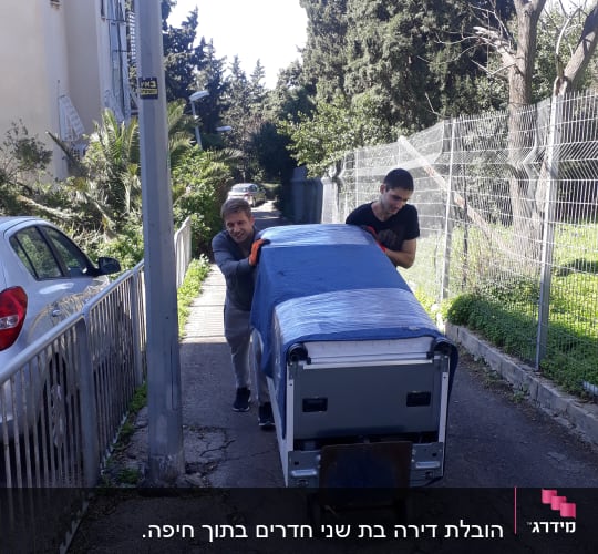 שני אנשים דוחפים עגלה עם חפץ מכוסה בבד כחול
